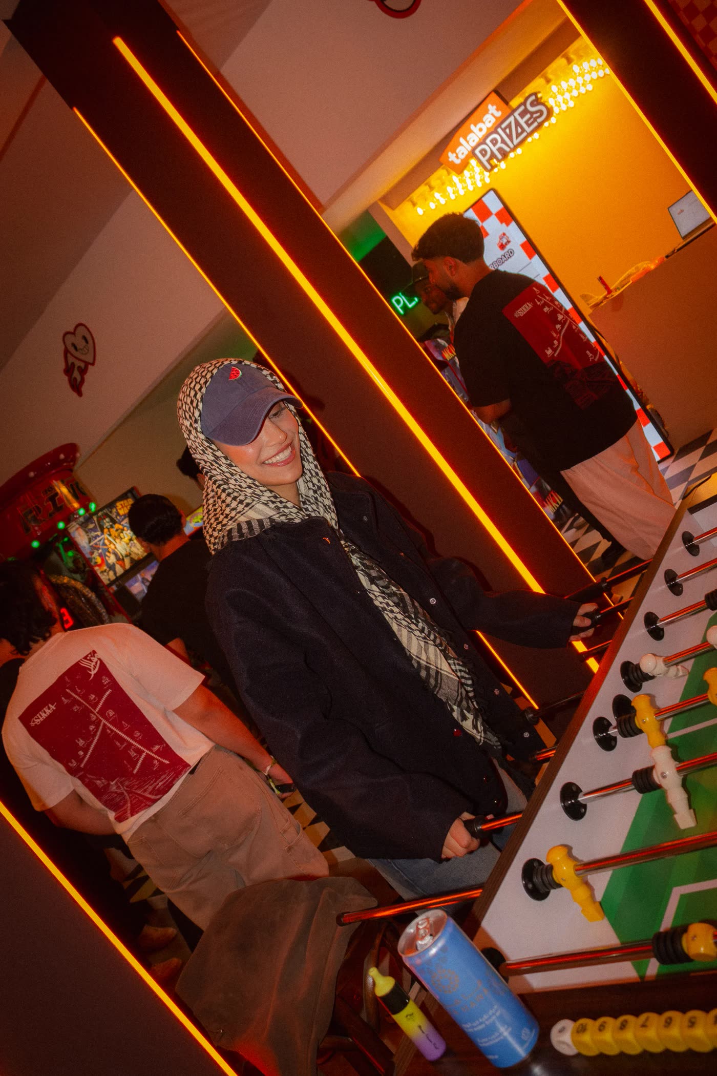 Hooded figures at a foosball table under orange light